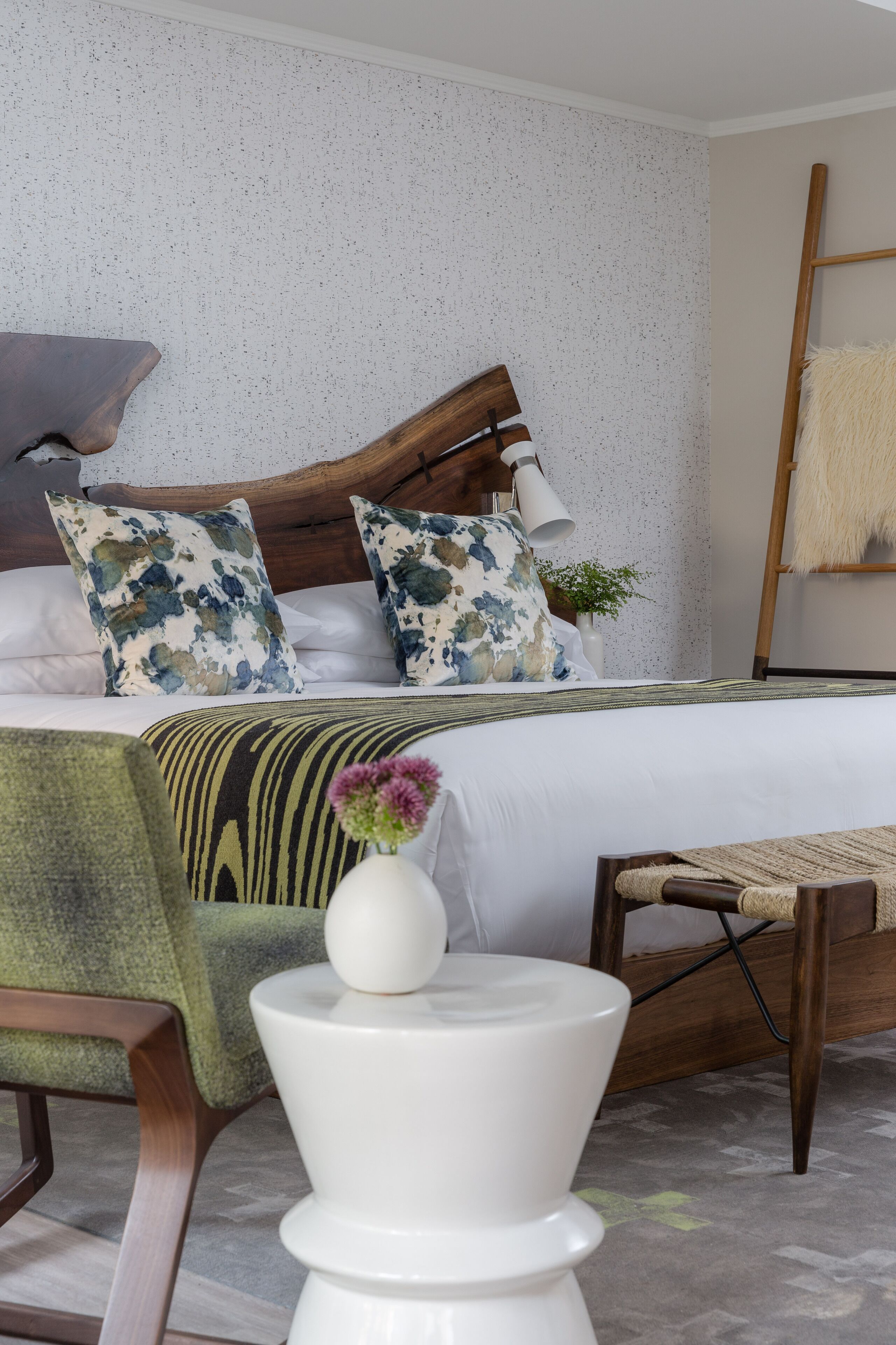 A neatly arranged bedroom with a wooden bed frame, white bedding, and a green armchair.