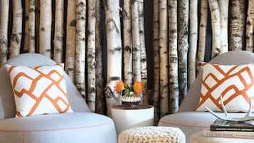 A living room with a birch bark wall, two grey sofas with patterned cushions, a small wooden stool, and a white fluffy rug.