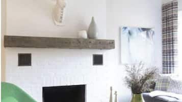 Ein modernes Wohnzimmer mit Kamin in Weiß, einem grünen Sessel und einem grauen Sofa.