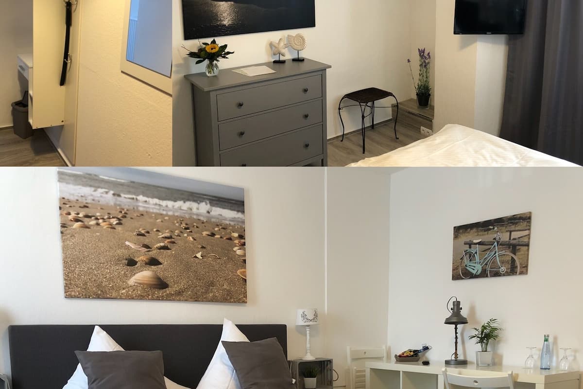A hotel room with a bed, a dresser, a TV, a small table, and a painting of a beach scene.