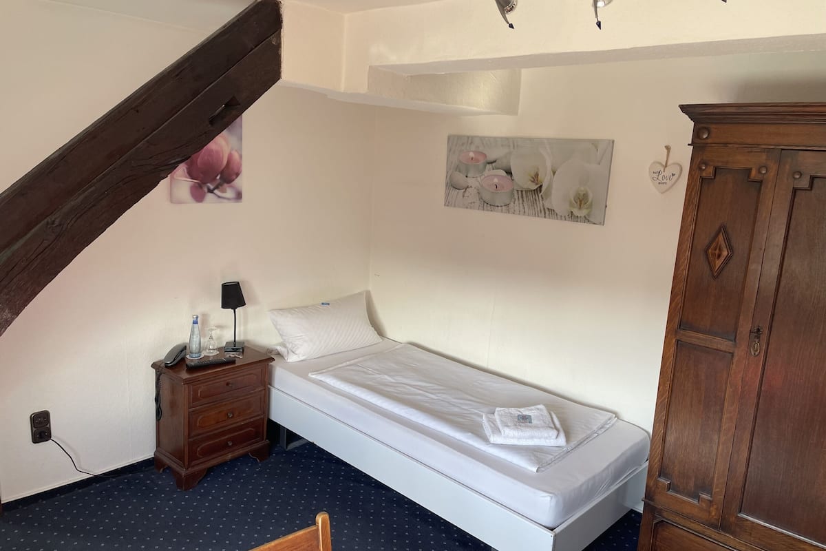 A bedroom with a single bed, a wooden nightstand, a small cabinet, and a painting on the wall.