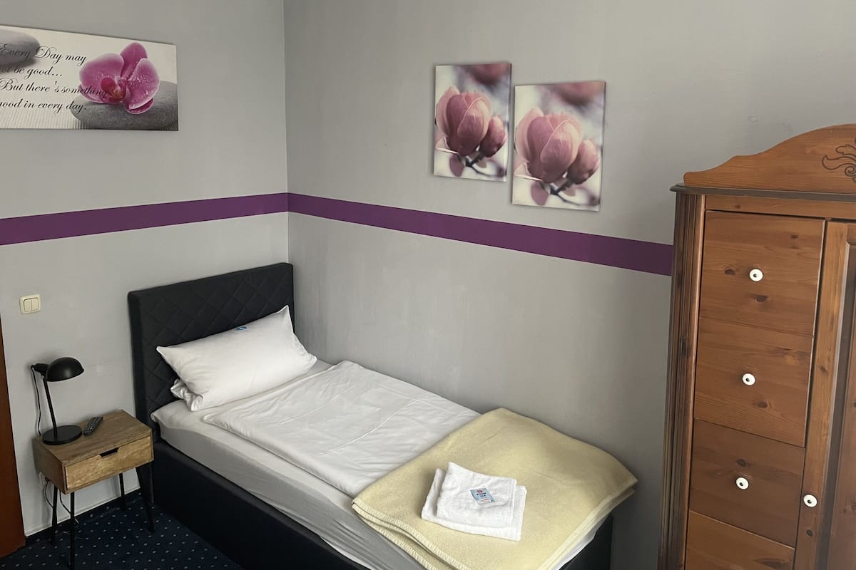 A neatly made bed with white linens, a wooden nightstand with a lamp, and a wooden wardrobe.