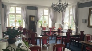 A dining area with multiple tables and chairs, potted plants, and a chandelier. - Hotel Jägerhof Kettwig (Essen)
