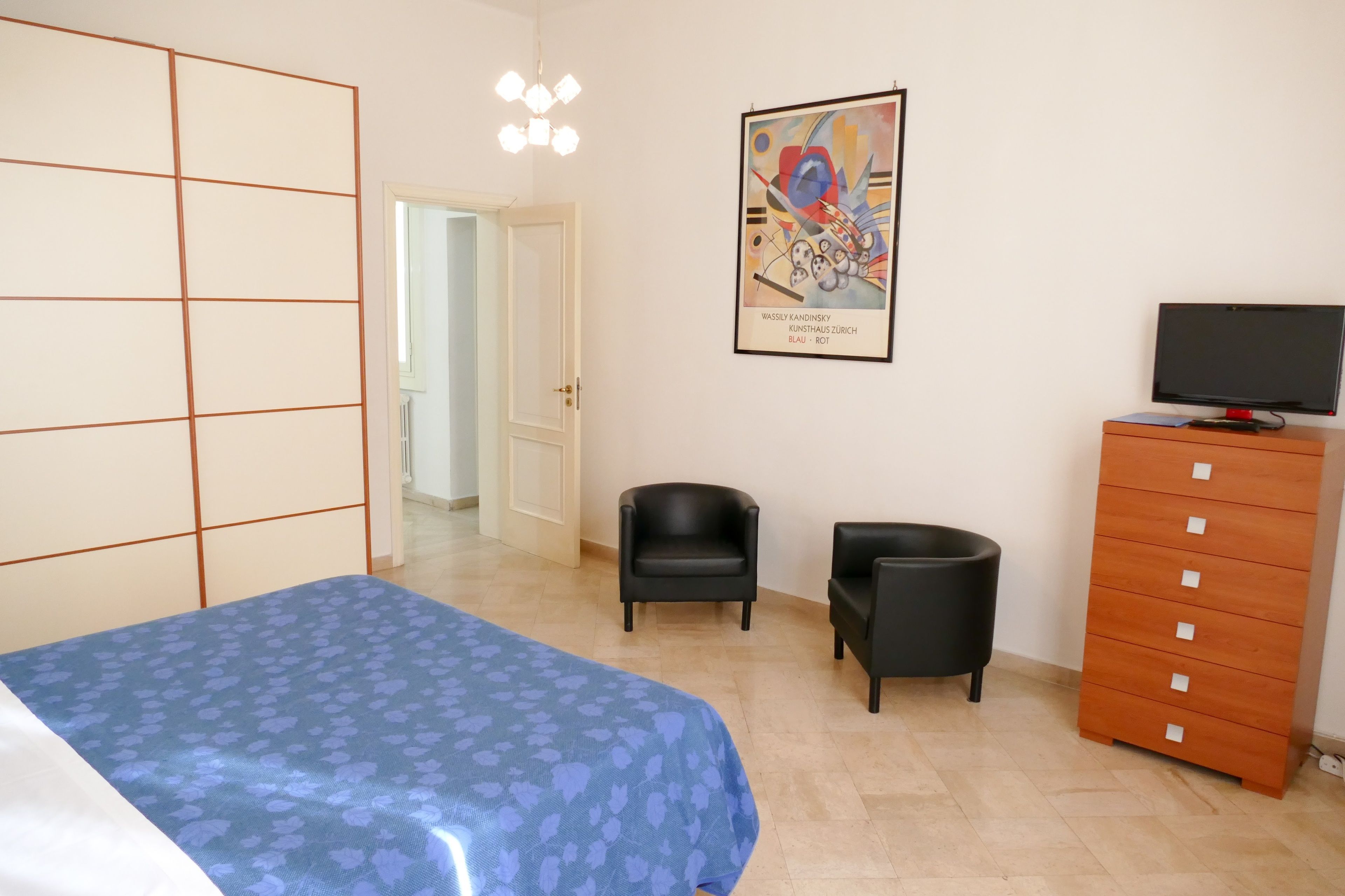 A bedroom with a bed, a dresser, a chair, and a television.