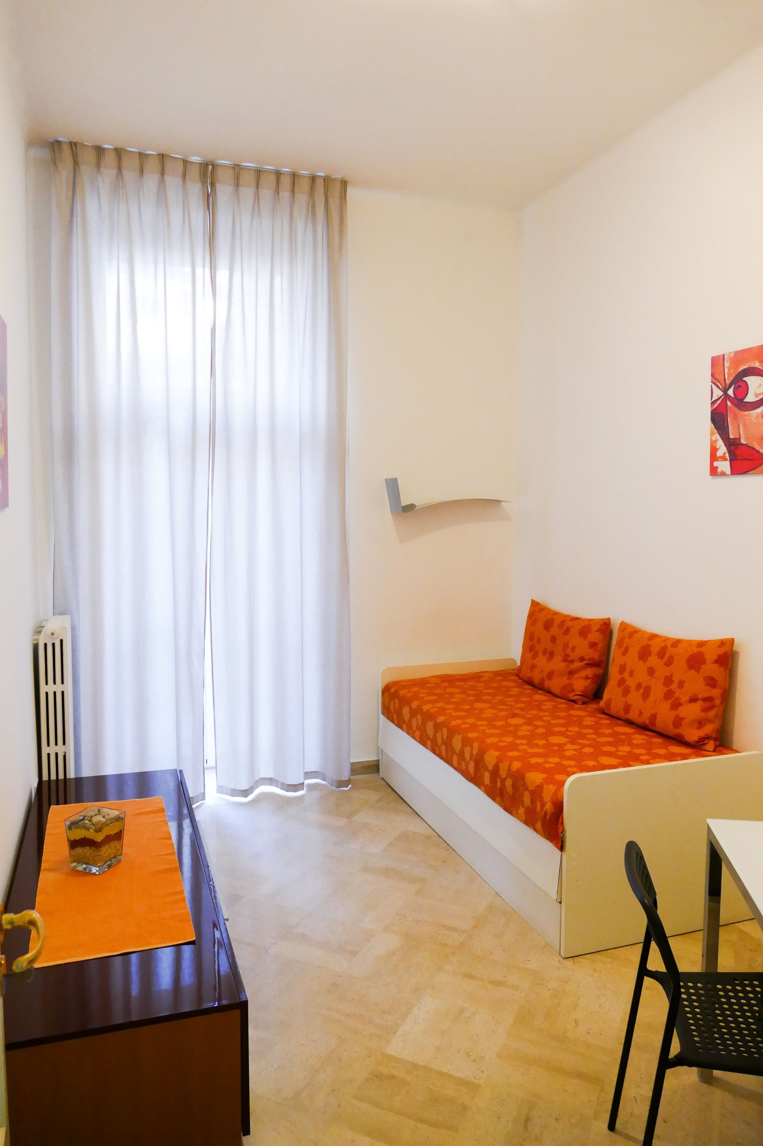 Un apartamento pequeño de una sola habitación con cama, escritorio, silla y radiador.