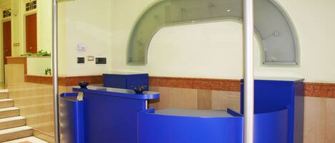 A reception area with blue reception desks, a curved glass partition, and a staircase in the background.
