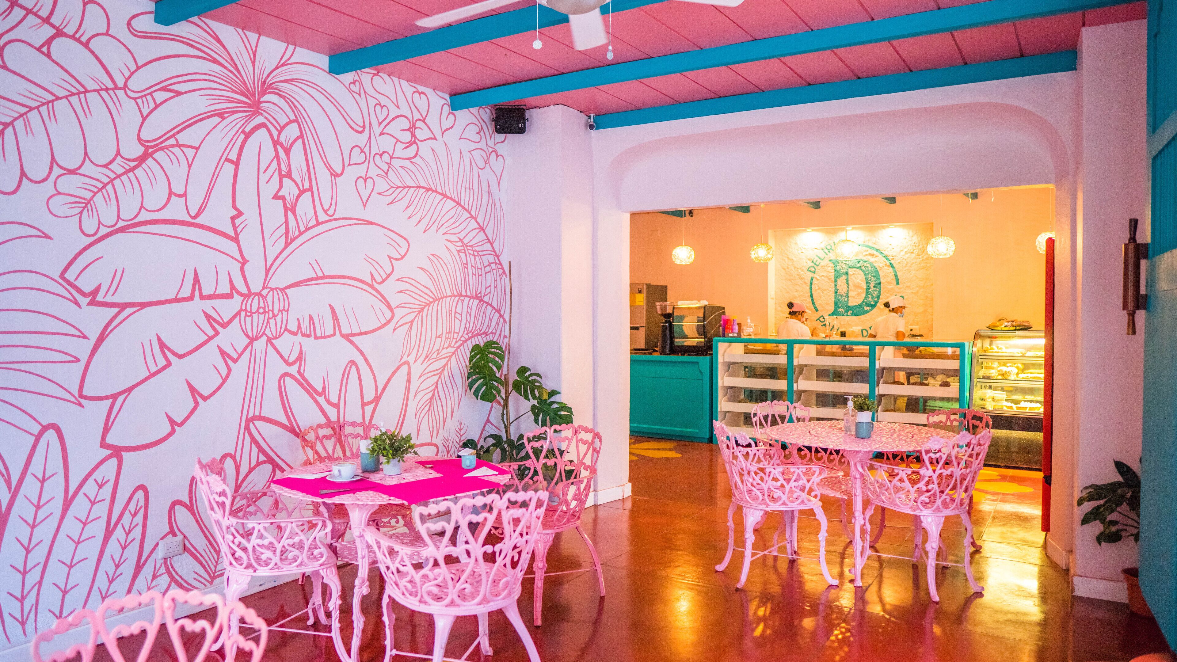 A restaurant interior with pink chairs, a table with a pink tablecloth, and a wall with a floral pattern.