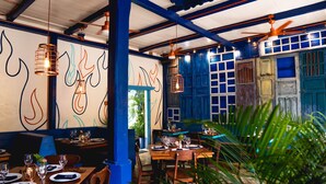 Un restaurante con mesas dispuestas para comer, paredes azules y lámparas colgantes.
