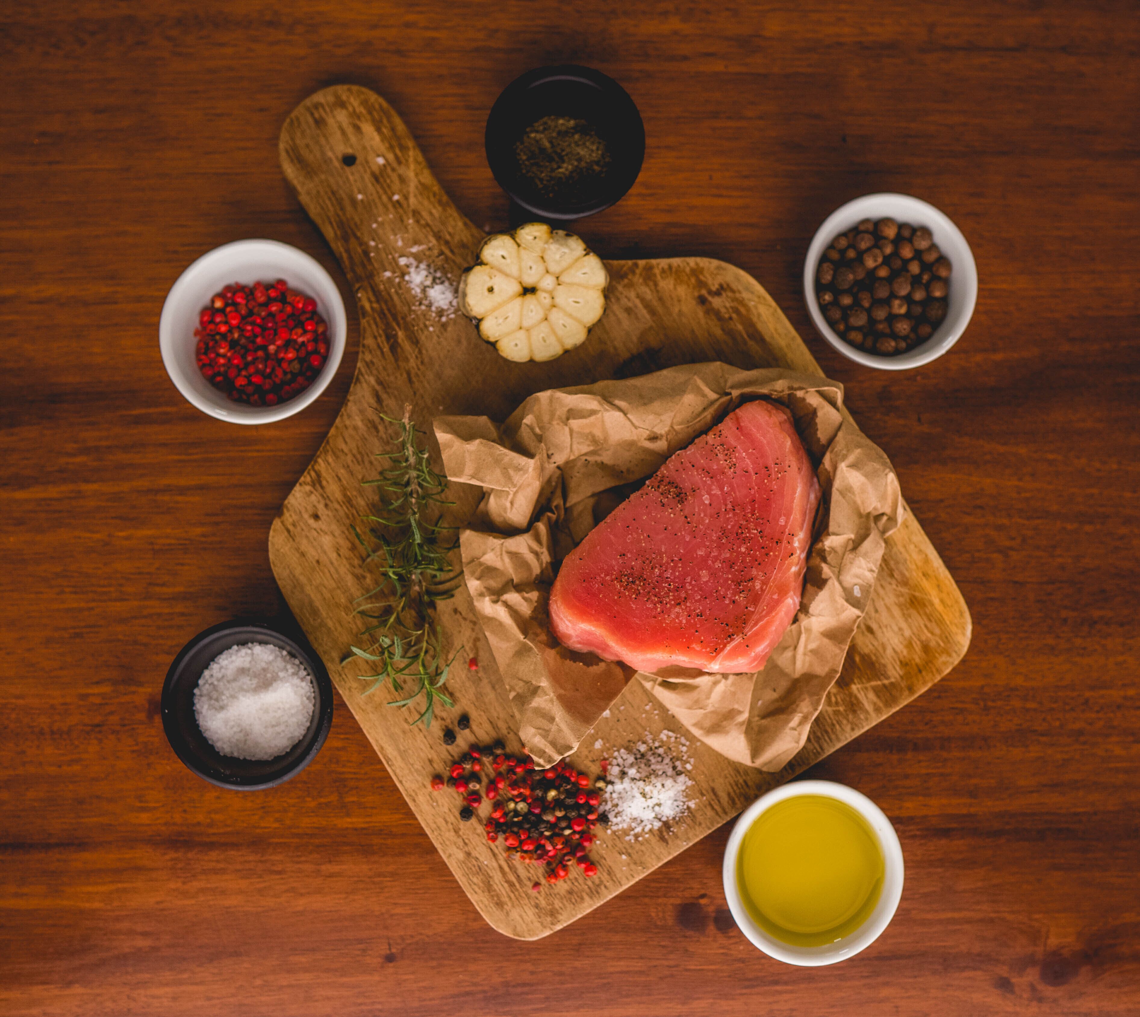Une planche à découper en bois avec de la viande crue, des herbes et des épices.