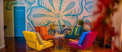 A room with vibrant, colorful chairs, a small round table, and a wall with a large, abstract mural.