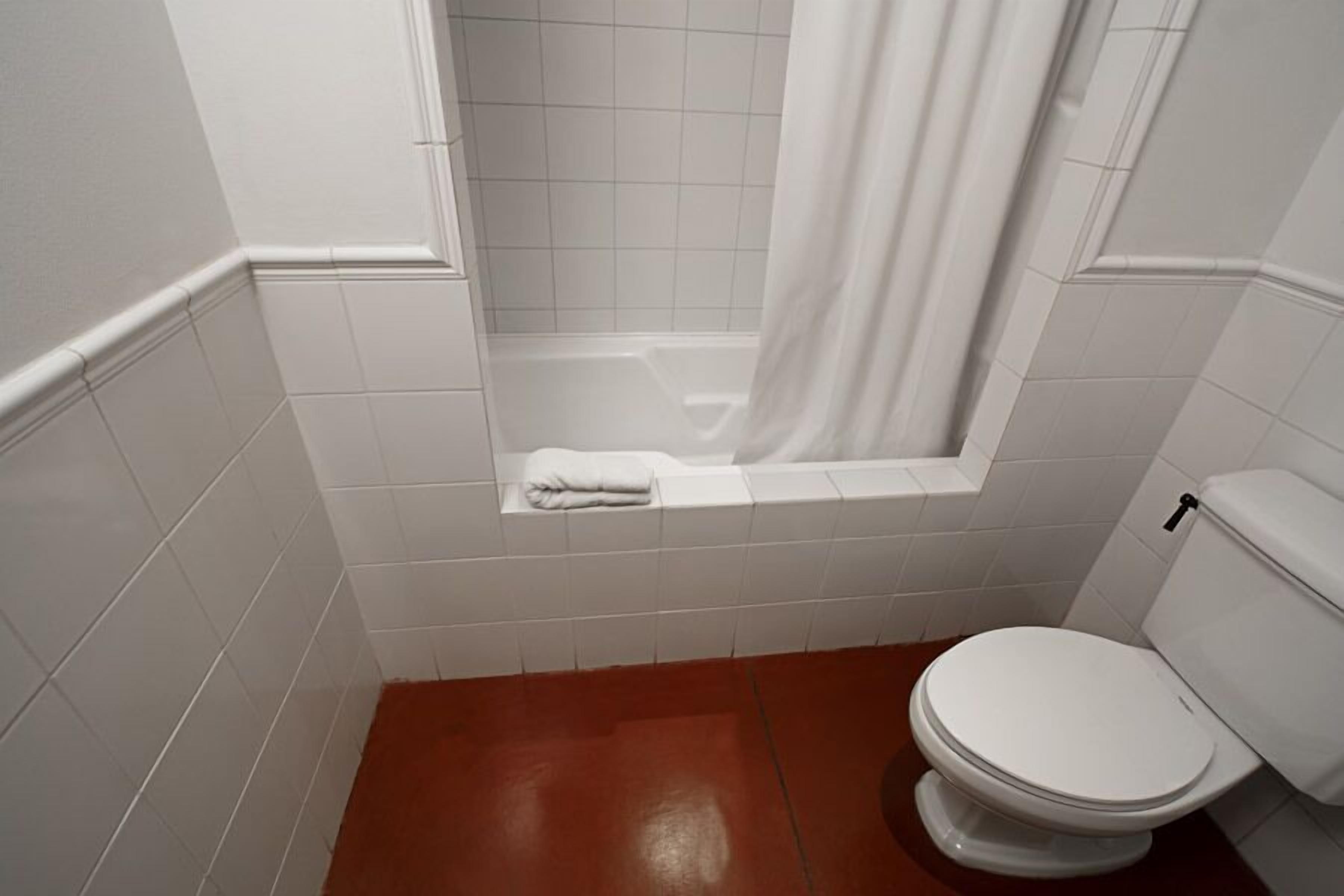 A bathroom with a white toilet, a bathtub with a white shower curtain, and white tiled walls.