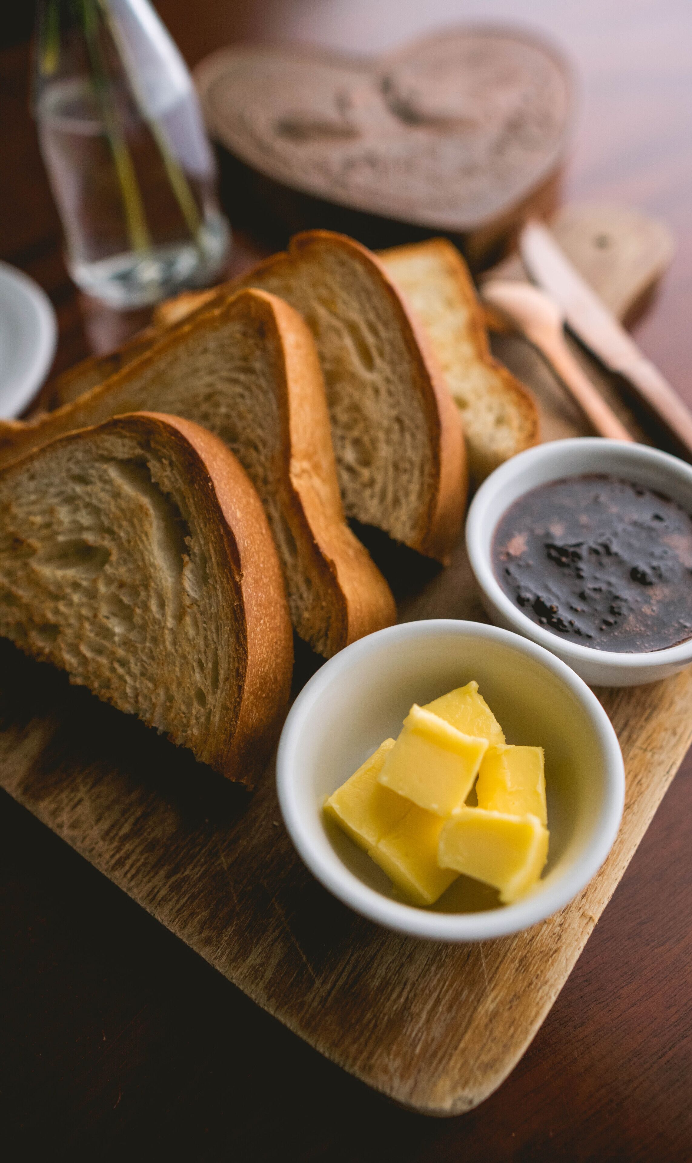 Slices of bread on a wooden board with two small bowls containing butter and jam.