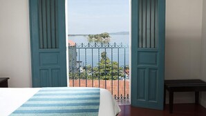 Un dormitorio con cama, un balcón que ofrece vistas a un lago y una isla, y una puerta con diseño decorativo.