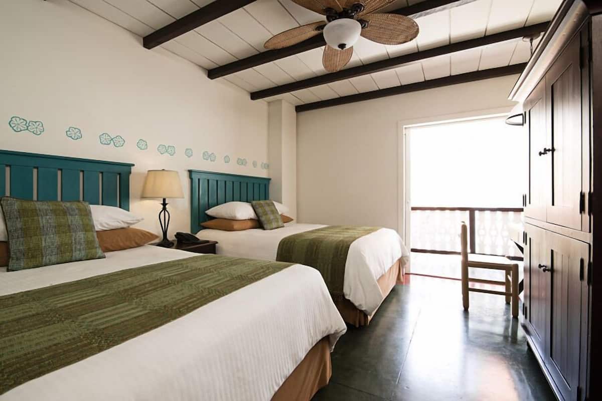 Una habitación con dos camas, ventilador de techo, lámpara y vistas al exterior.