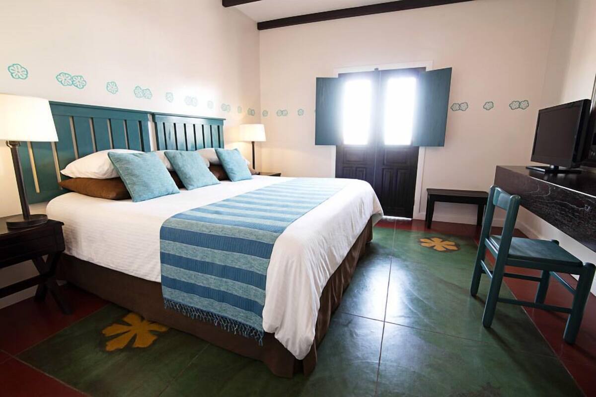 Una habitación de hotel con una cama, dos mesitas de noche, un escritorio, una silla y un televisor.