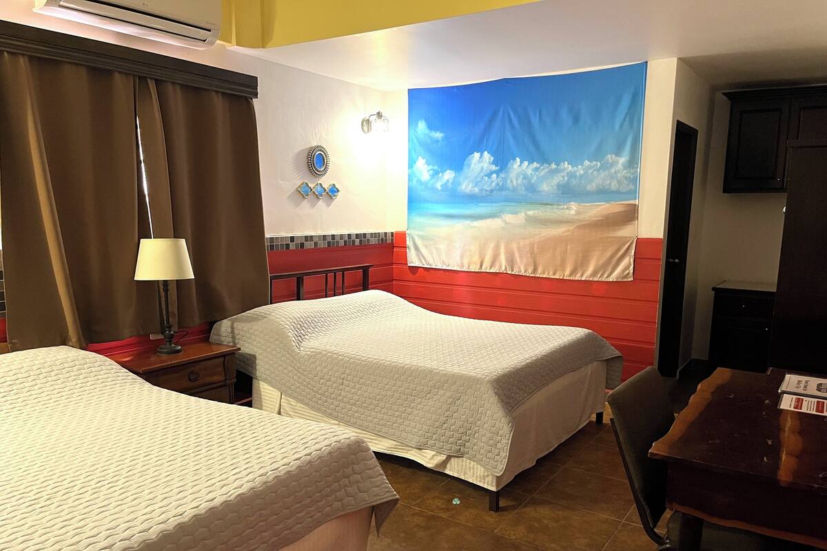 Ett hotellrum med två sängar, en röd accentvägg, ett stort fönster med utsikt över stranden och ett skrivbord med en stol.