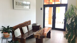 Un espacio de sala con un banco de madera, una mesita y una planta en maceta.