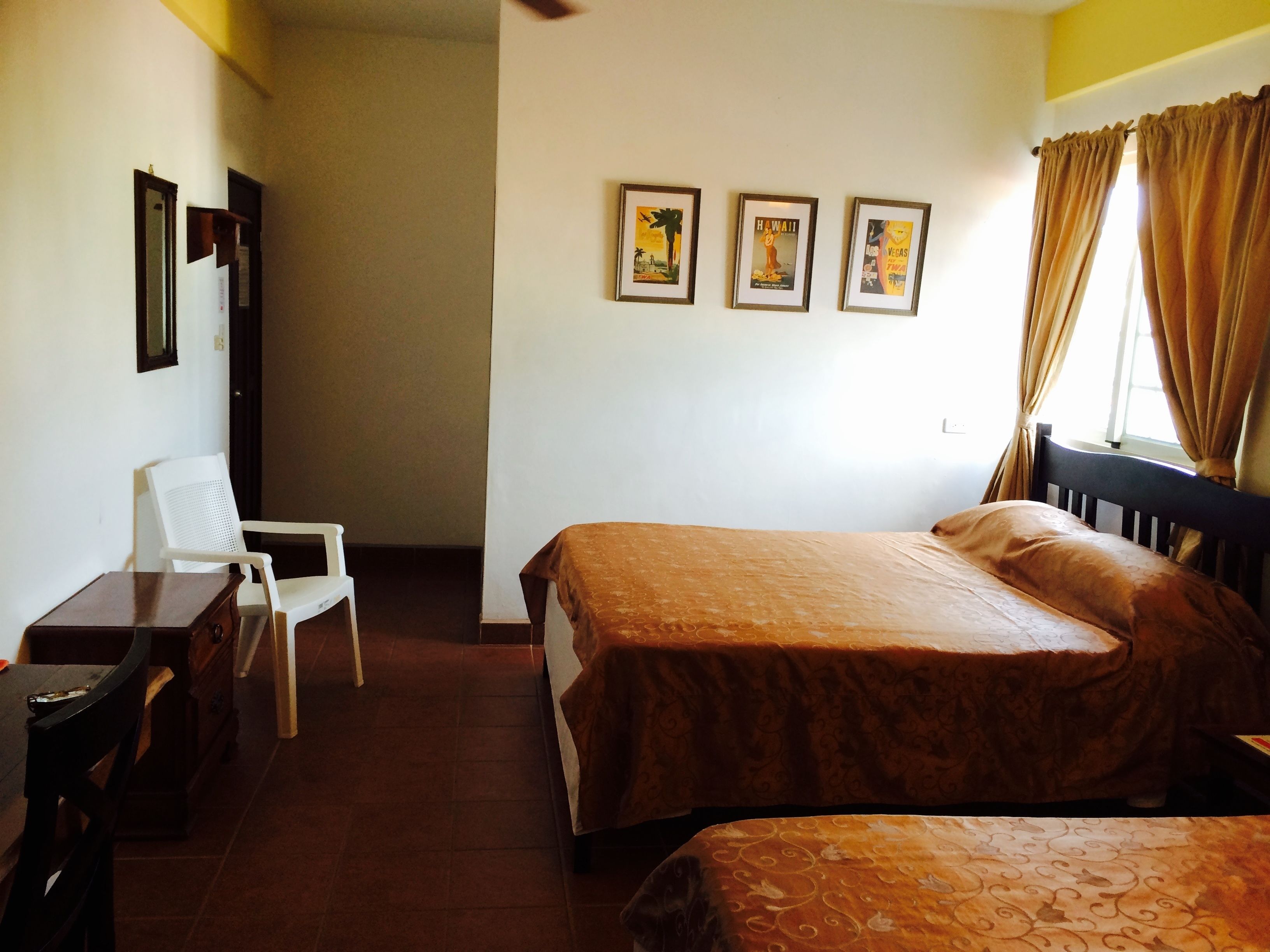 Une chambre d’hôtel avec un lit, une chaise, une petite table et trois tableaux encadrés accrochés au mur.