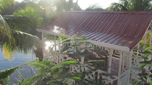 Una estructura de madera con techo de metal, rodeada de abundante vegetación y palmeras.