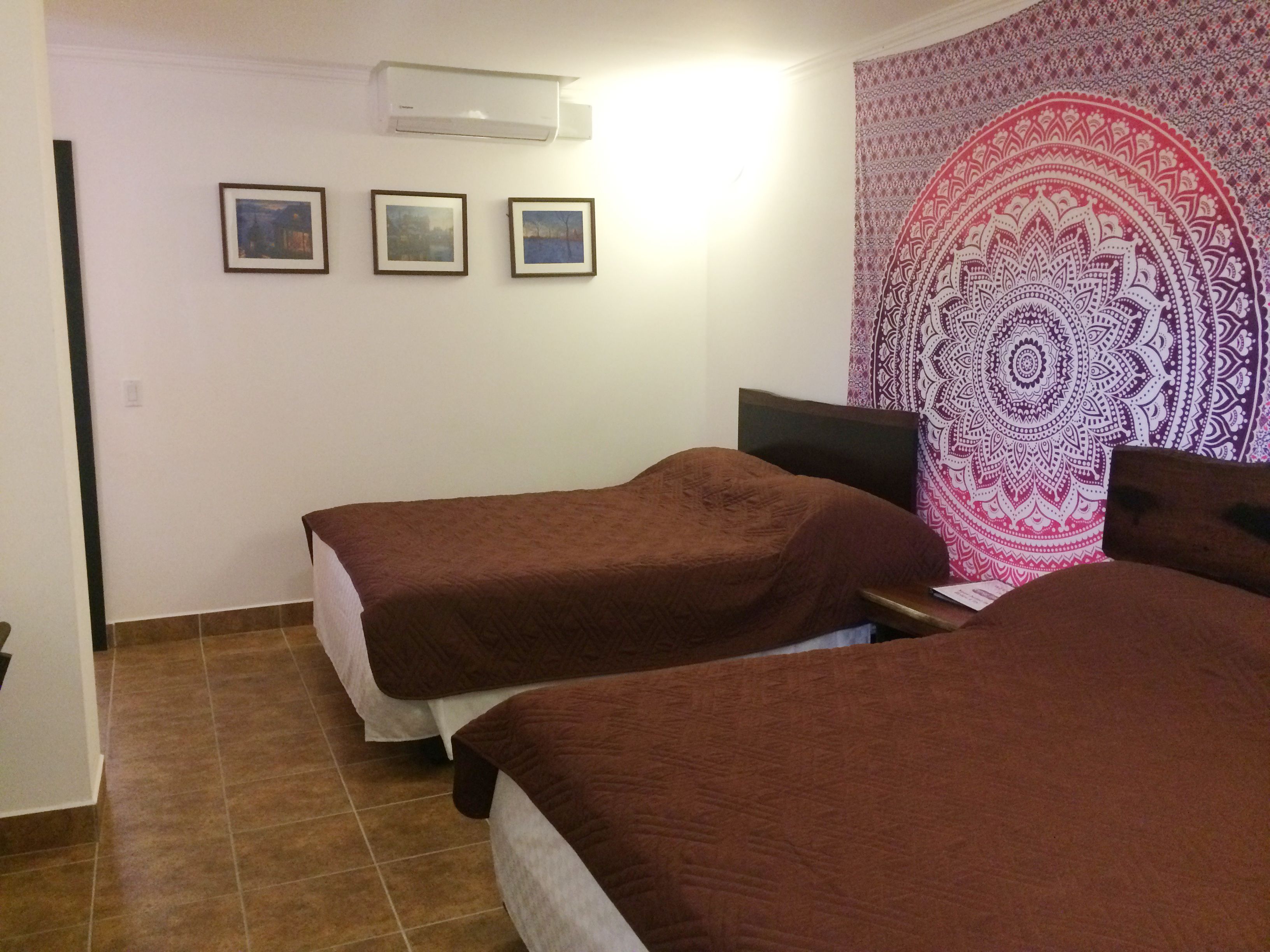 Een kamer met twee bedden, een wandtapijt en drie ingelijste foto's aan de muur.