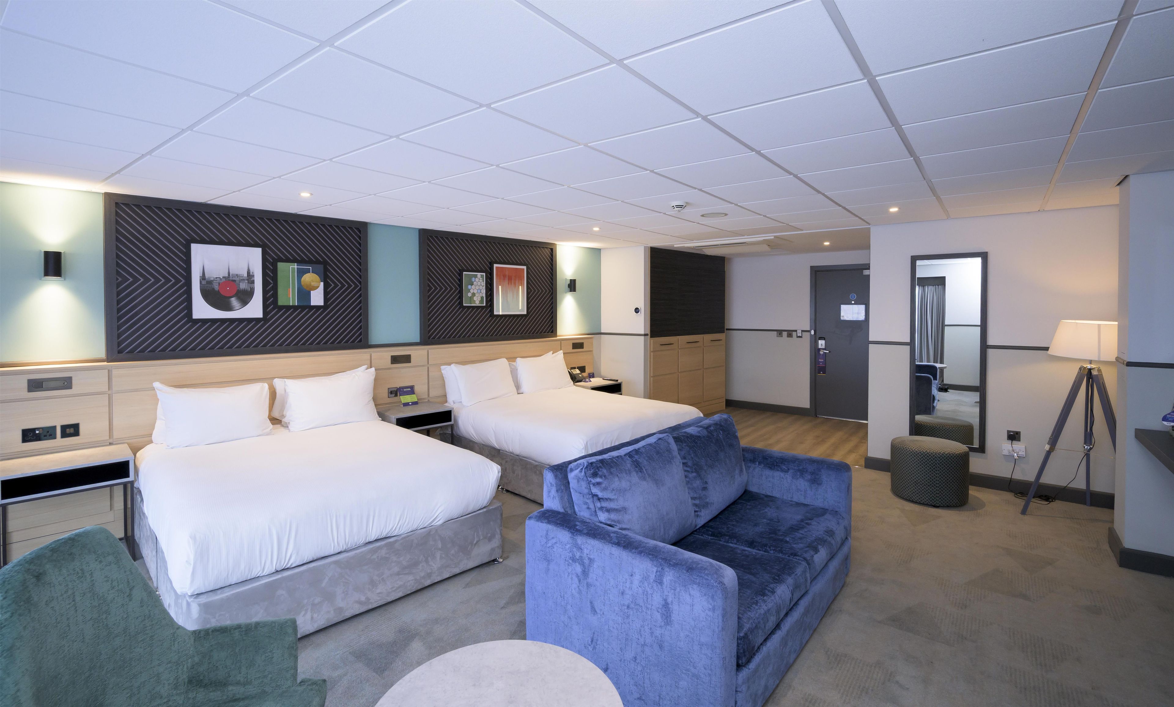 Habitación de hotel con dos camas, un sofá, un escritorio y un espejo.