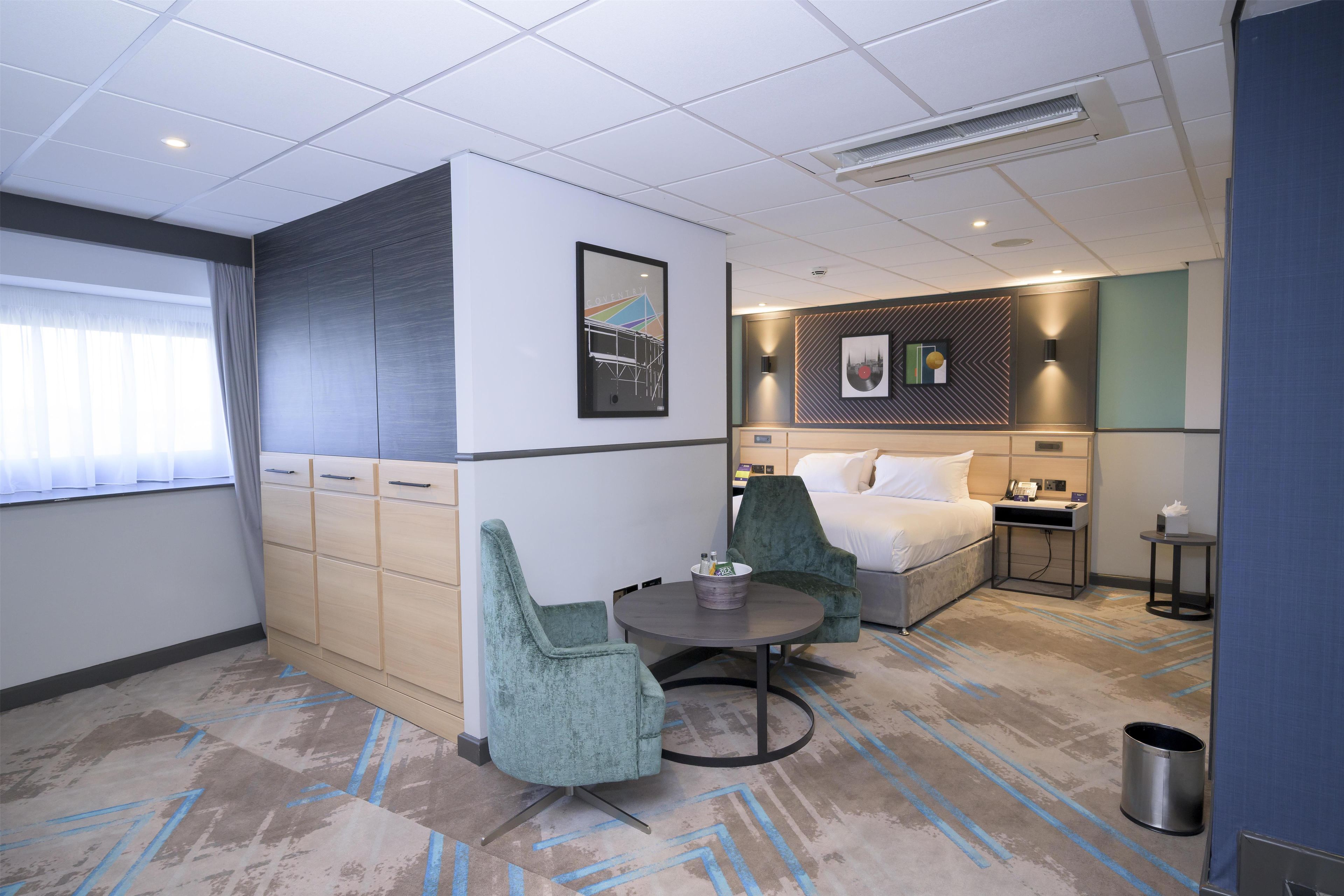 A hotel room with a bed, a desk, a chair, a small table, and a trash can.