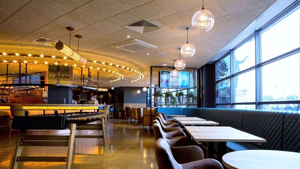 Um restaurante moderno com área de bar, assentos ao longo das paredes e grandes janelas que proporcionam luz natural.