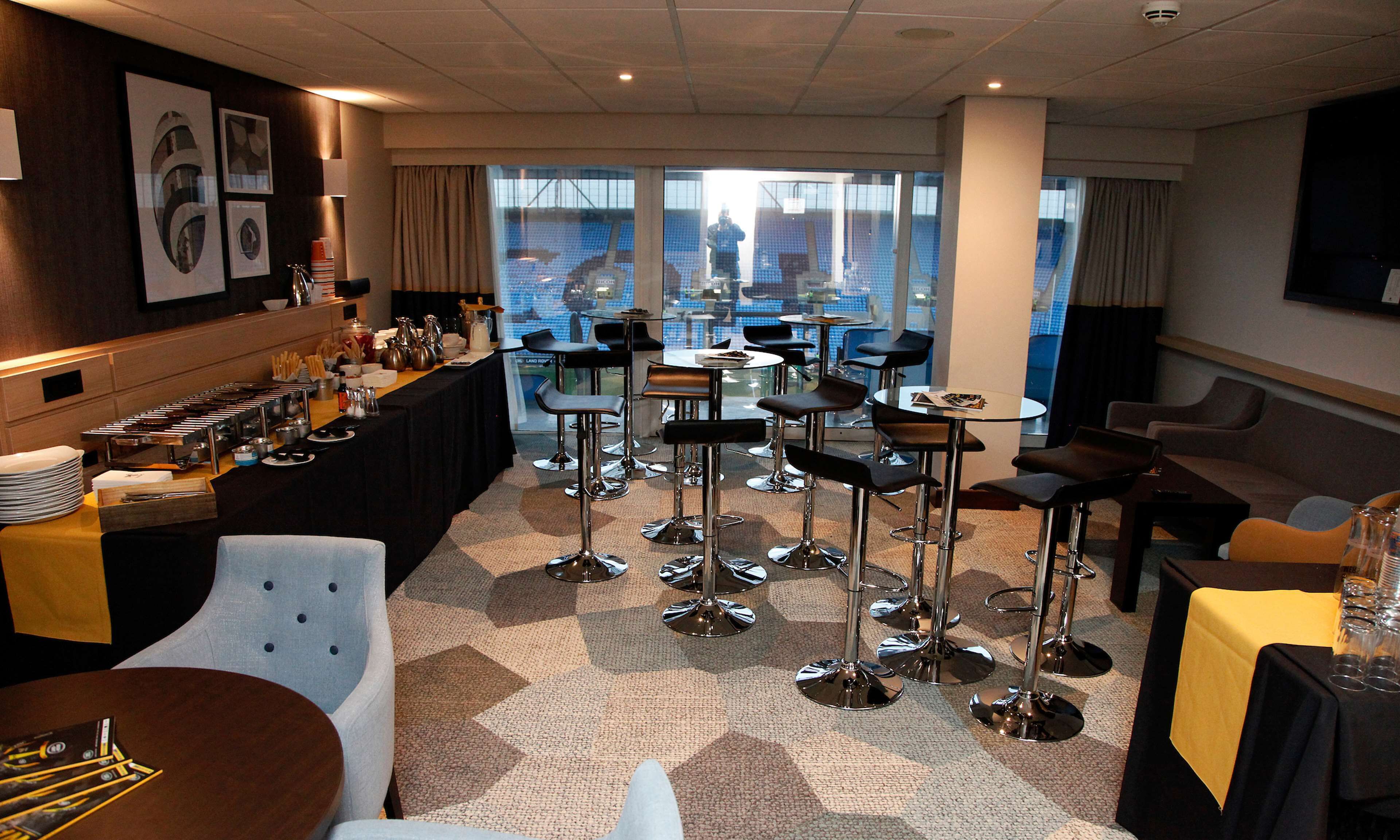Zona de bar del hotel con diversas opciones de asientos, un bufé y grandes ventanales con vistas.