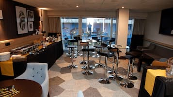 Zona de bar del hotel con diversas opciones de asientos, un bufé y grandes ventanales con vistas.