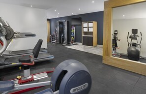 Un gimnasio moderno con diversos equipos de ejercicio, incluyendo cintas de correr, un banco de pesas y pesas libres.