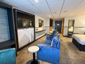 A hotel room with a sofa, a small round table, a bed, and a bathroom with a shower and toilet.