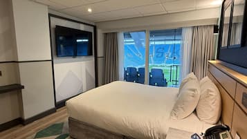 A hotel room with a large bed, a desk with a telephone, and a view of an empty stadium through the window.
