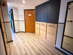 Een gang met een houten deur, een kledingkast met meerdere lades en een lichtgekleurde vloer.