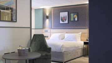 Una habitación de hotel con una cama, un sillón verde, una mesita y una pared decorada con cuadros.