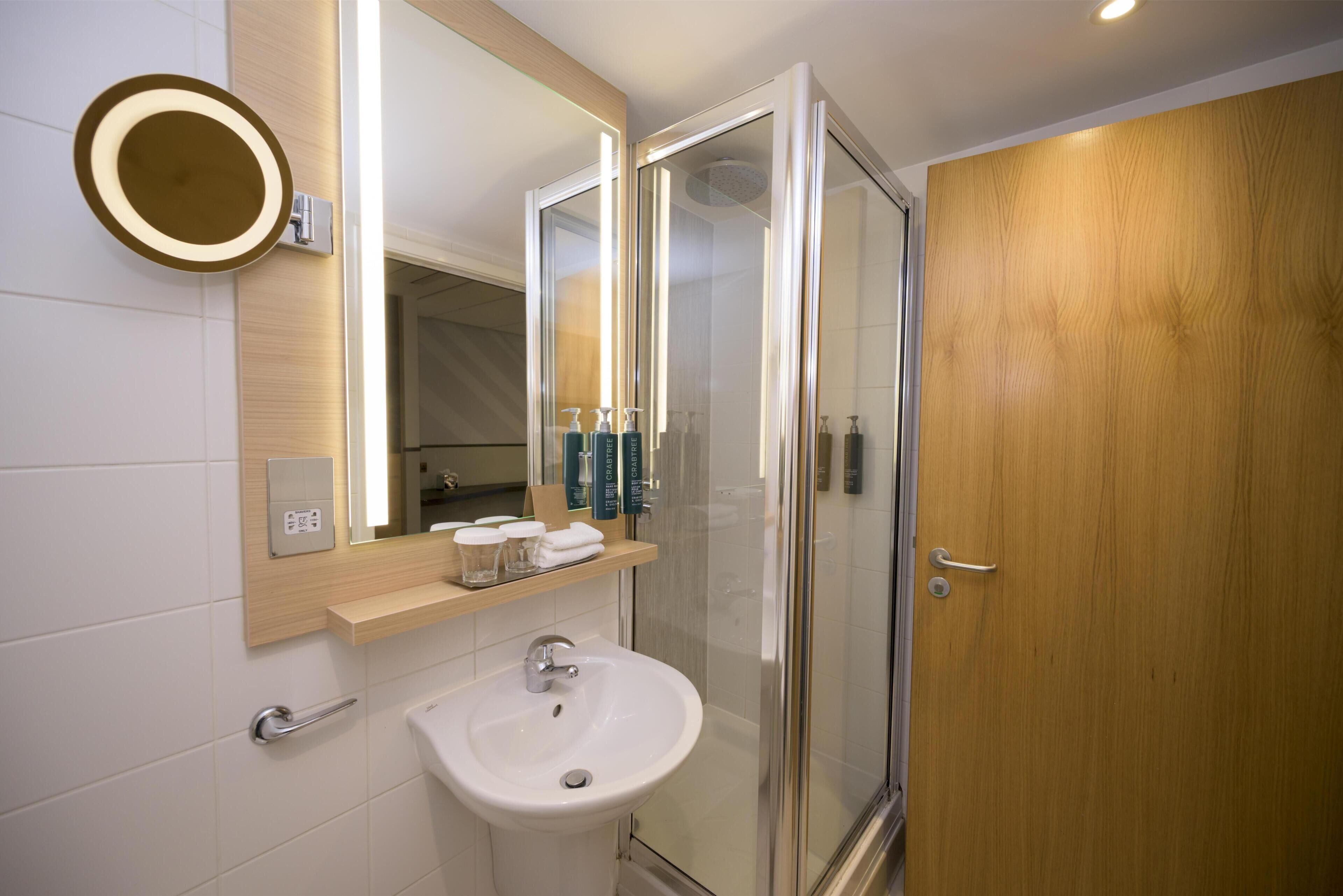 A bathroom with a sink, mirror, and shower.
