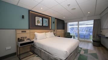 A modern hotel room with a large bed, bedside tables, a desk, and a view of a stadium.
