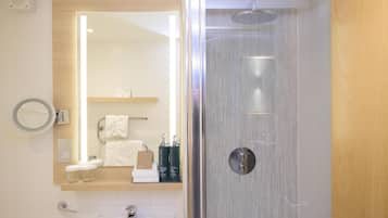 Une salle de bain moderne avec une douche à parois de verre, un miroir, un porte-serviettes et une étagère contenant des articles de toilette.