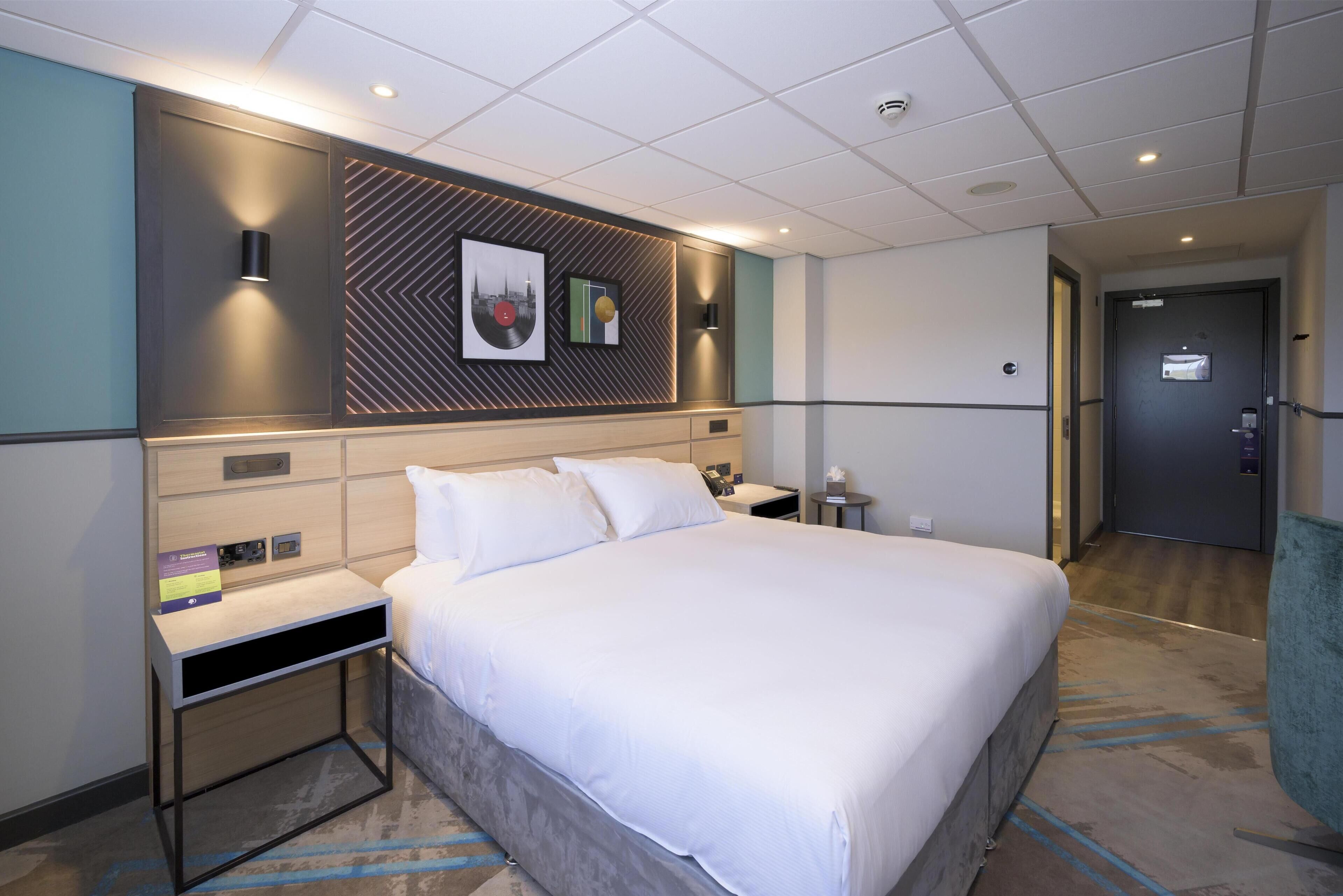 Una habitación de hotel con cama, mesitas de noche, una obra de arte en la pared y una puerta.
