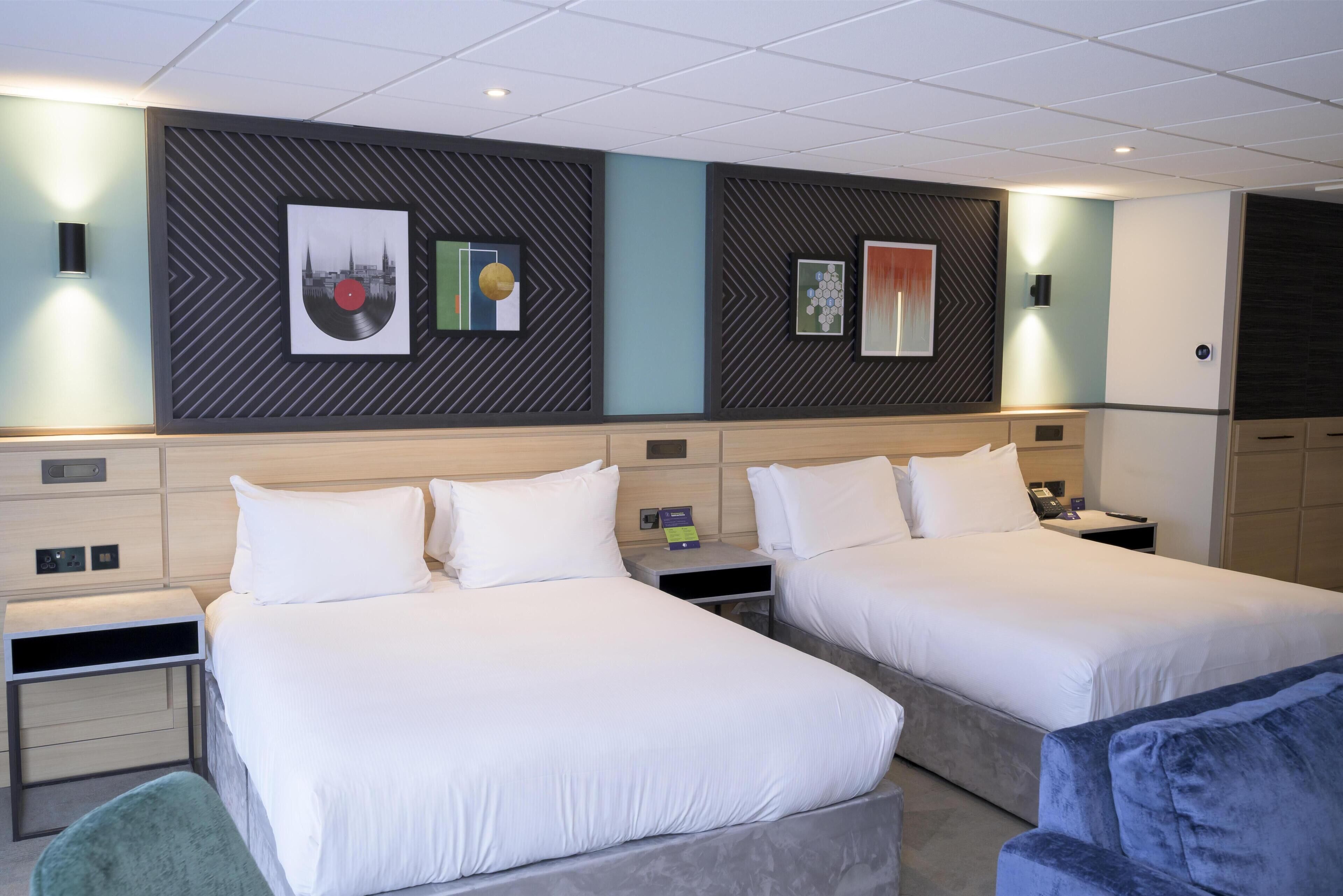 A hotel room with two beds, a desk, a chair, and artwork on the walls.