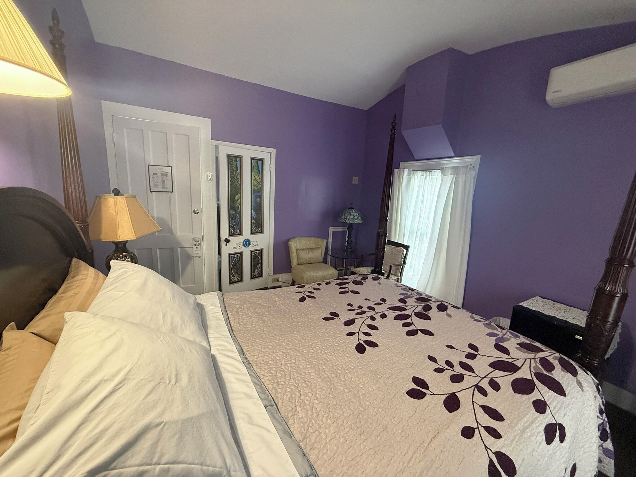 Un dormitorio con cama, una silla, un escritorio y una puerta con paneles de vidrio.