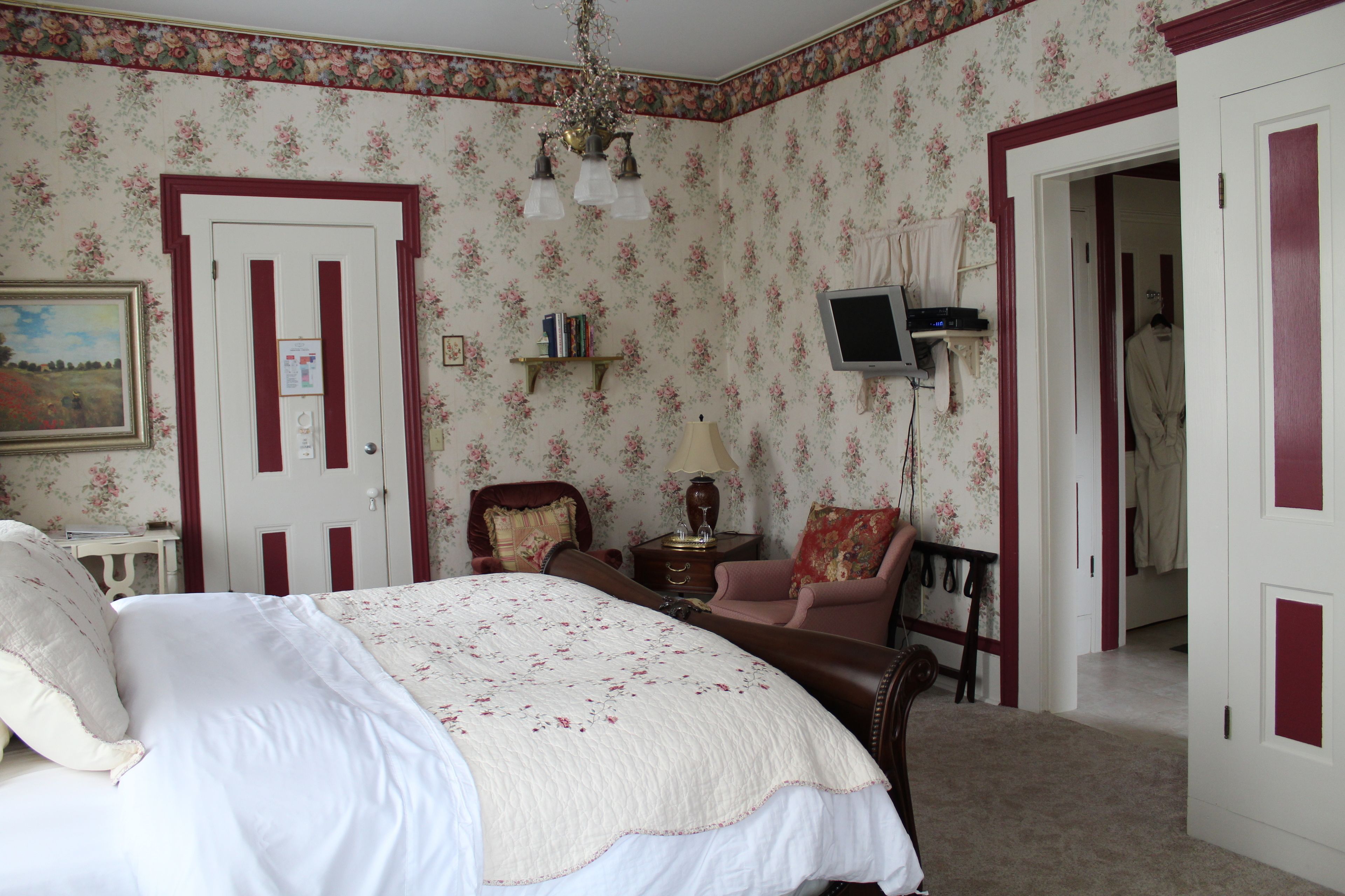A bedroom with a bed, a chair, a TV, and a door.