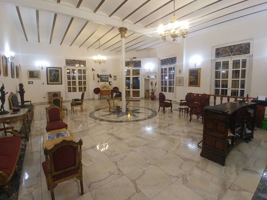 A spacious lobby with a marble floor, wooden furniture, and a central chandelier.