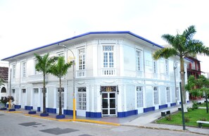 A white building with blue trim and decorative windows, featuring a central entrance with a door and a small porch area. - Apart Hotel Casa Morey (Iquitos)