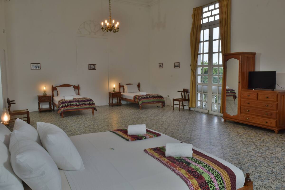 A spacious bedroom with two single beds, a large bed, a wooden dresser, a television, and a chandelier.