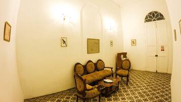 A room with a patterned floor, a sofa, two armchairs, a small table, and a door with a sign.