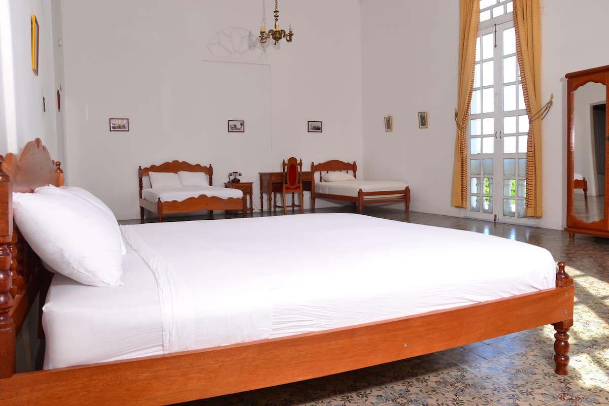 A spacious bedroom with a large bed, two smaller beds, a wooden chair, a mirror, and a chandelier.