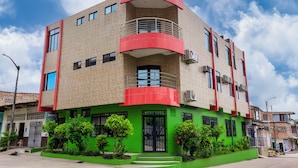 Un edificio de varios pisos con base verde y detalles en rojo, que cuenta con balcones y unidades de aire acondicionado.