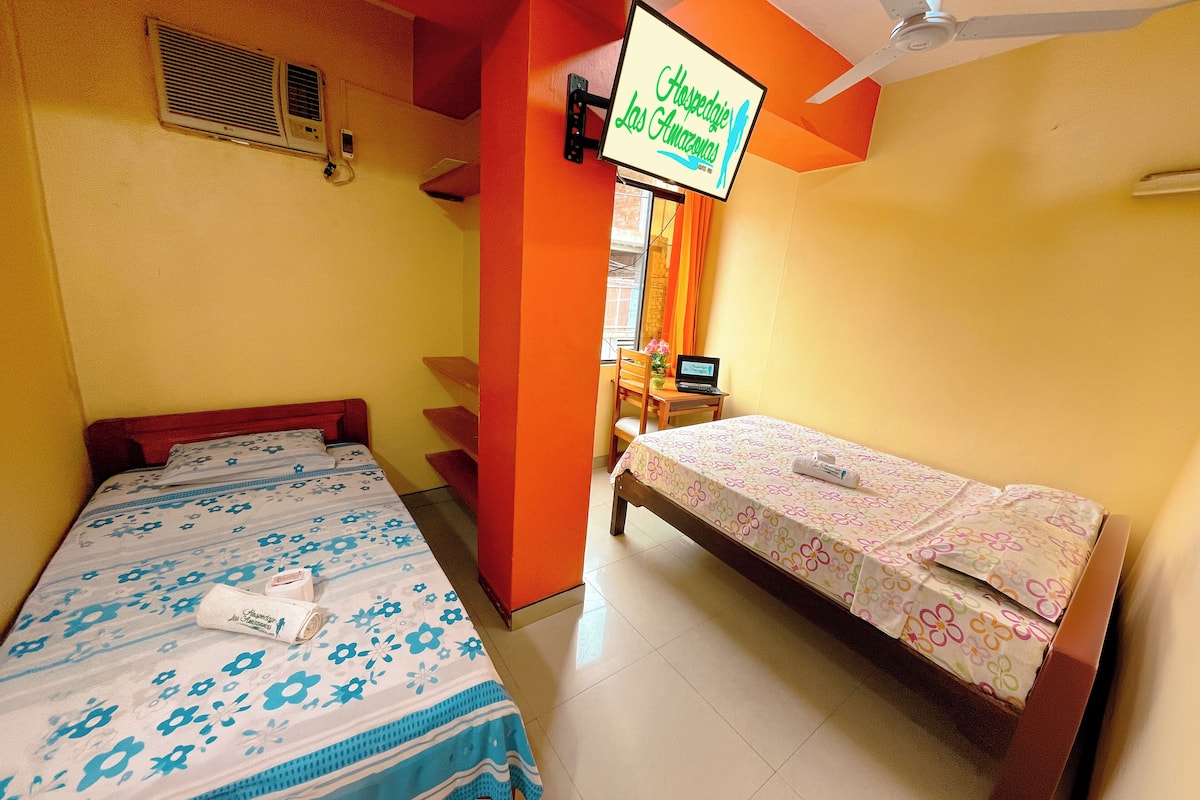 A hotel room with two beds, a TV mounted on the wall, and a window with curtains.