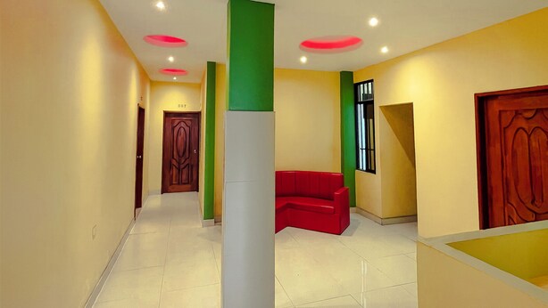 Un pasillo moderno con un sofá rojo, una puerta de madera y un pilar verde.