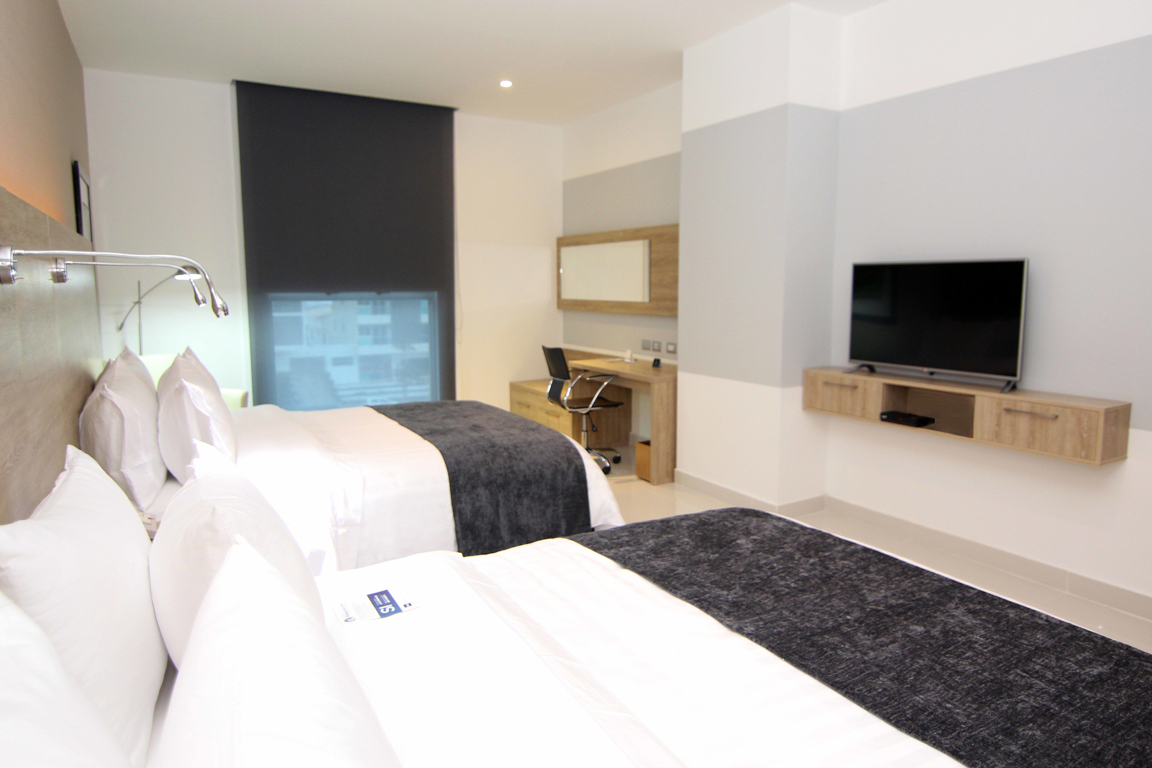 A modern hotel room with a large bed, a desk, a television, and a window with a view.